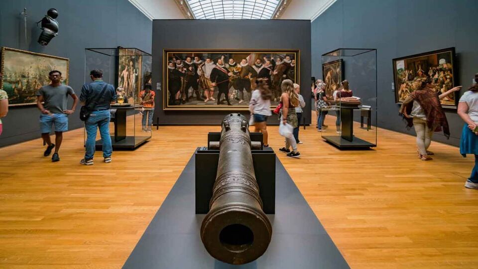 People in a large gallery/hall. a large cannon is in the middle of the room