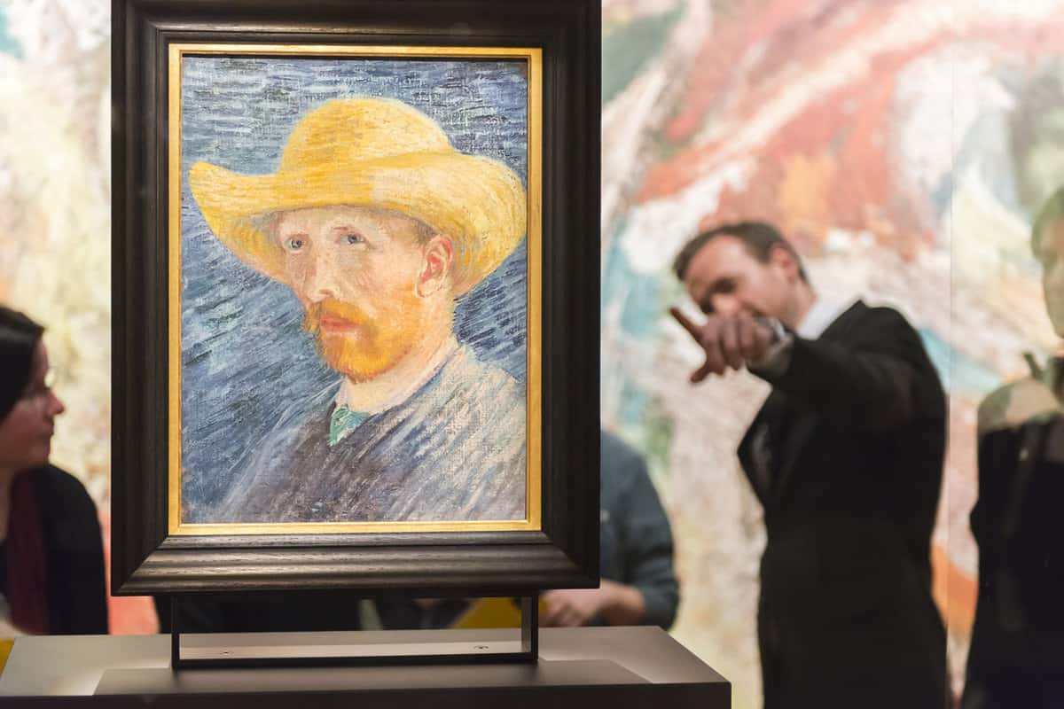 Close up of a painting with a man pointing to it in the background