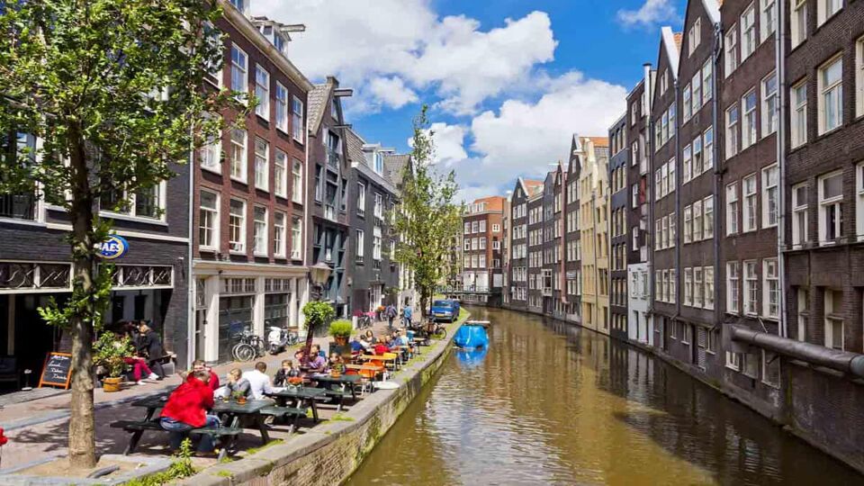 People sitting at tables having coffee and drinks on the banks of a canal surrounded by townhouse