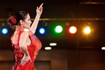 Sexy flamenco dancer performing her dance in a red long dress, arm up.