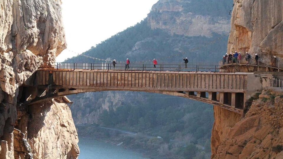 Tourists wearing helmets walk across a bridge between two mountains