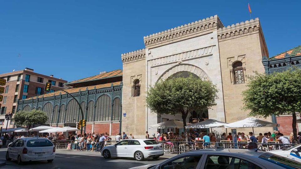 Exterior of the market with people waiting and cars parked