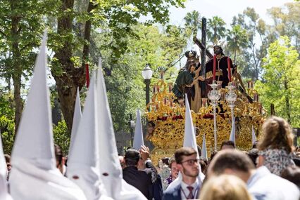 People wearing large pointed white hoods in procession, with a large religious statue held in the background