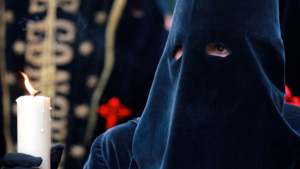 Close up of person wearing black pointed hood holding a candle