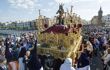 Procession of a gold and velvet carrier with a statue of Jesus, through a crowd in daytime