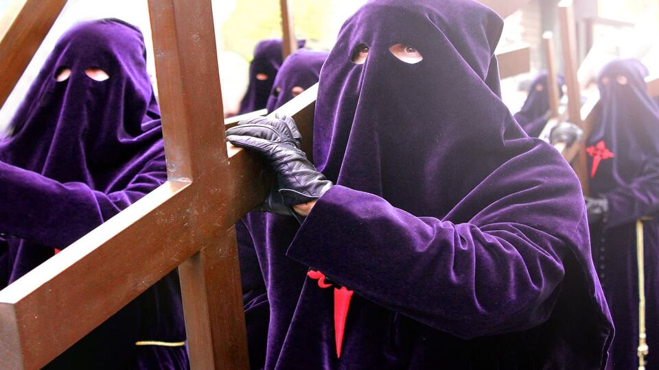 People wearing pointed purple hoods and purple robes carry crucifixes