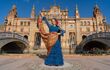 Woman in a blue flamenco dress posing before an ornate stone building in Seville