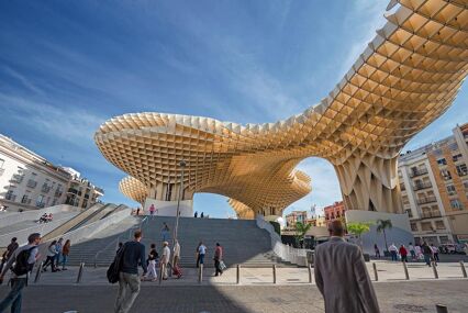 Large wooden slatted structure in a strange curving shape, providing a roof about the forecourt