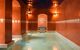 A long pool inside a hammam, surrounded by red walls with handing lanterns