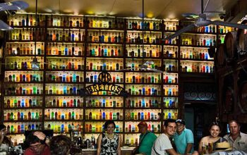 Patrons of Brettos bar smile at the camera. The bar behind them is lined with rows of multicoloured bottles up to the ceiling