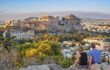 Two people sit atop Filopappou Hill and look over the city