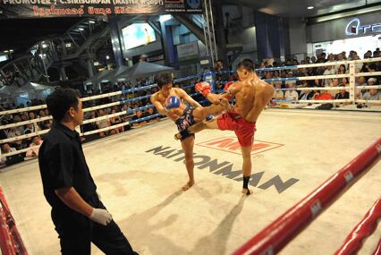 Two men competing in a kick boxing match inside of the ring, surrounded by onlookers