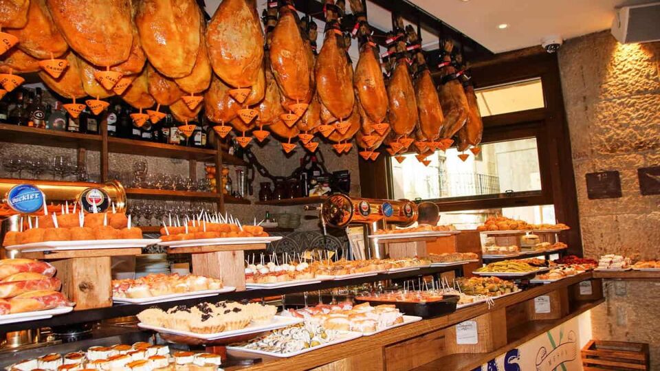 view of a food shop selling pintxos on counter and hams hanging down