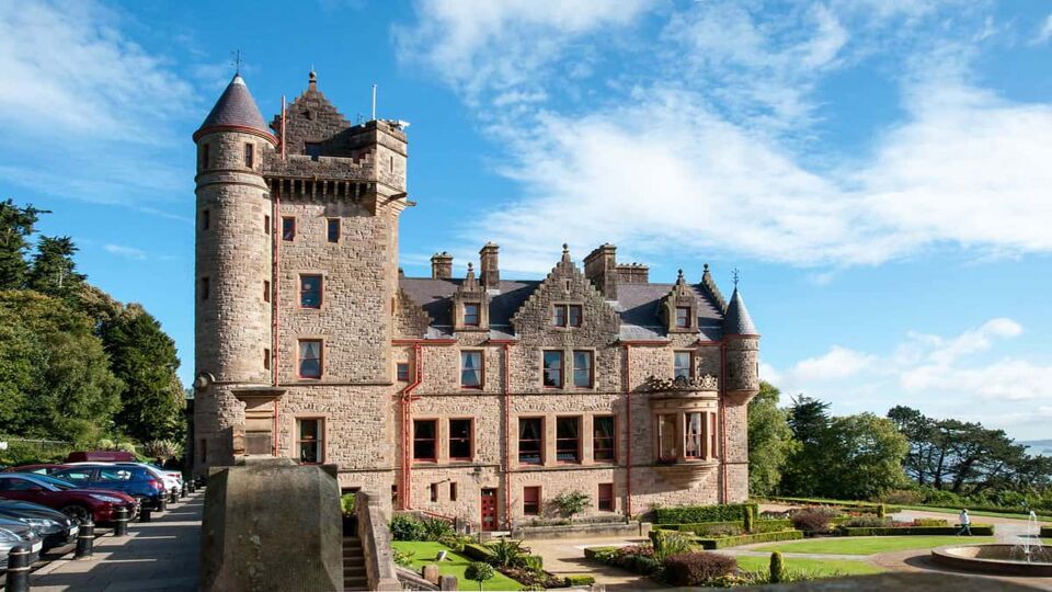 Exterior view of the small red brick castle. Belfast Castle (1860), is just outside the city, offers city views, landscaped gardens and local history at the visitor centre