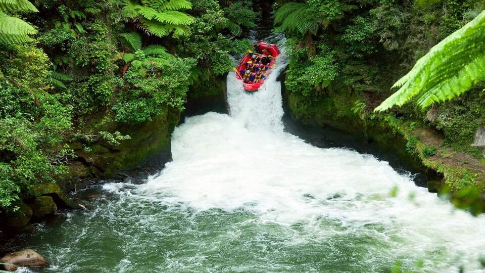 Raft going down a steep waterfall drop in rainforest of New Zealand