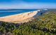 A large dune with greenery on one side and the sea on the other