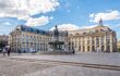 People walk by a fountain in front of a grand building