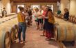 Tourists listening to a tourguide explain while in a wine cellar full of wine barrels
