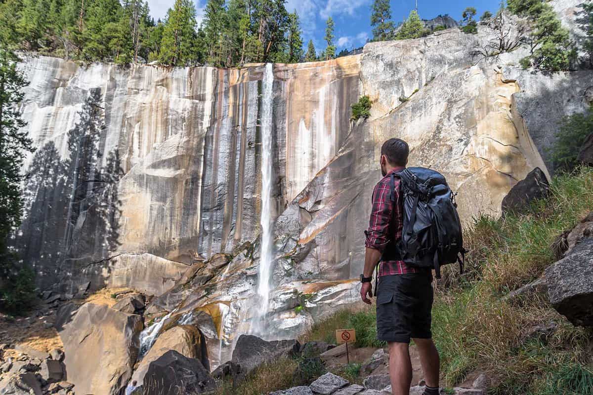 Man standing looking at a waterfall over a granite cliff