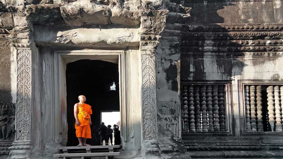 Lone monk in orange sash stands at a building entrance