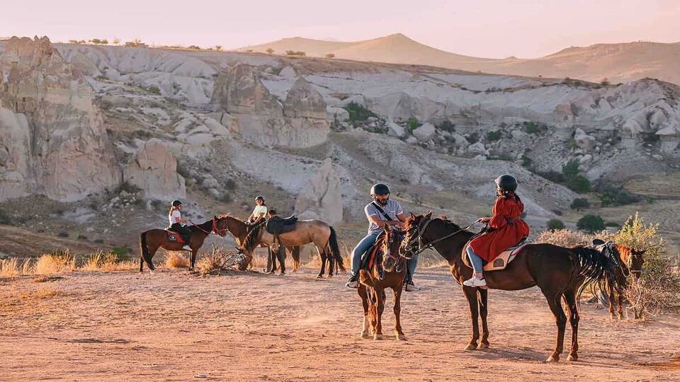 horse riders crossing a cappadocian landscape at sunset