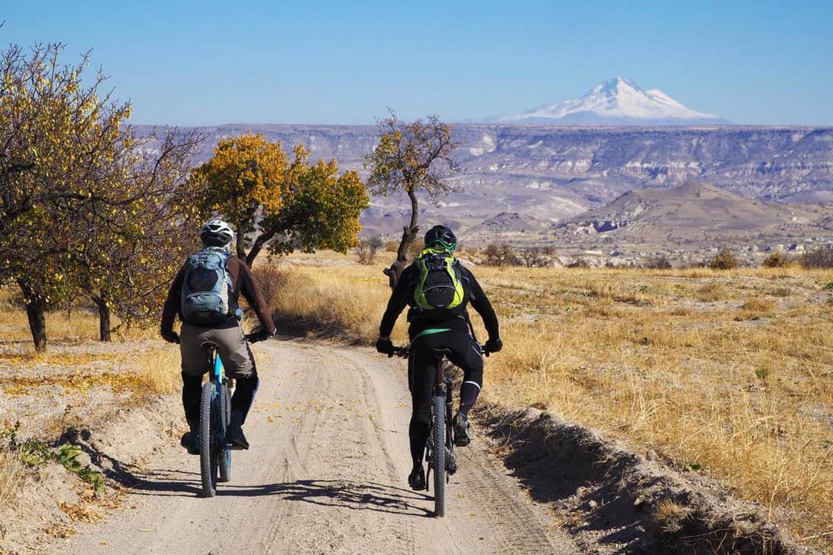 Two people biking down a mountain with the silhouette of mountains in the background.