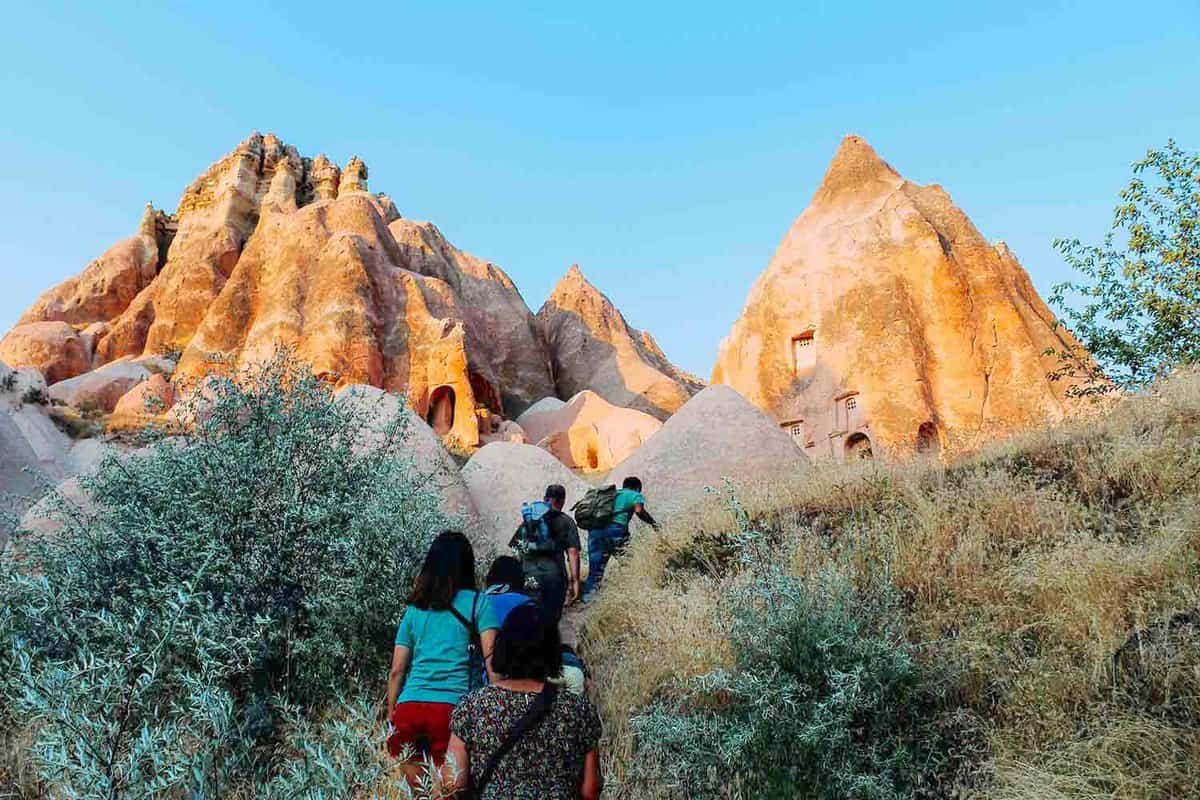 People walking up a steep mountain with tall pointy rocks on either side. Taken at sunset.