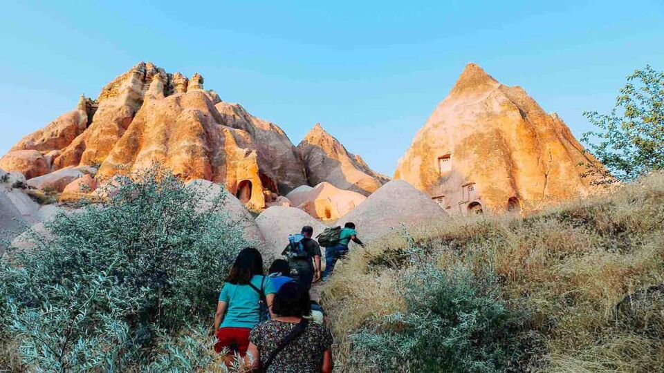 People walking up a steep mountain with tall pointy rocks on either side. Taken at sunset.