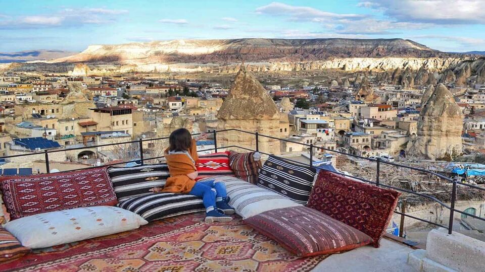 The girl sits on soft cushions on the open veranda and looks at the panorama of the city of Goreme, Cappadocia, Turkey