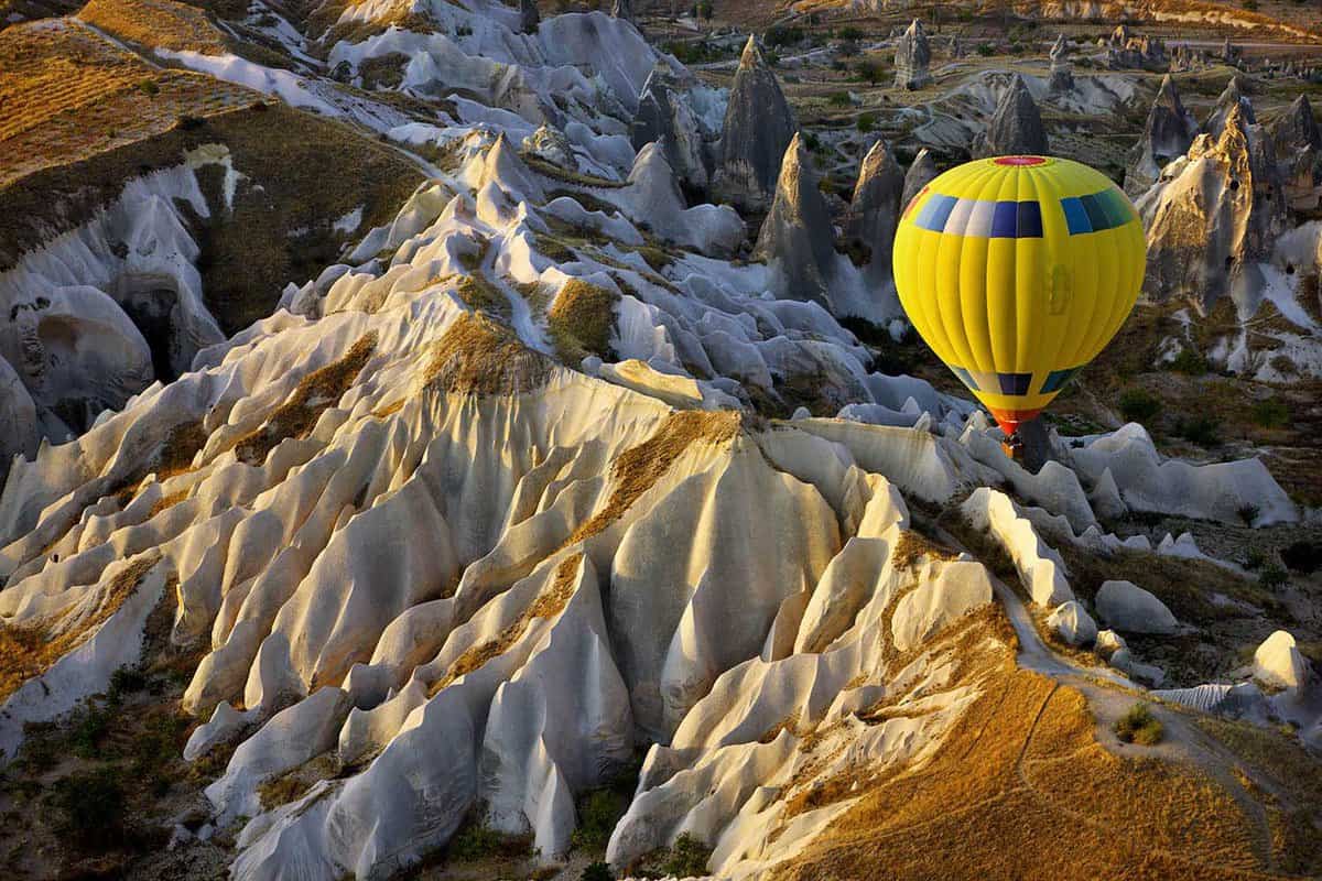 A yellow hot air balloon over jagged orange rocks.