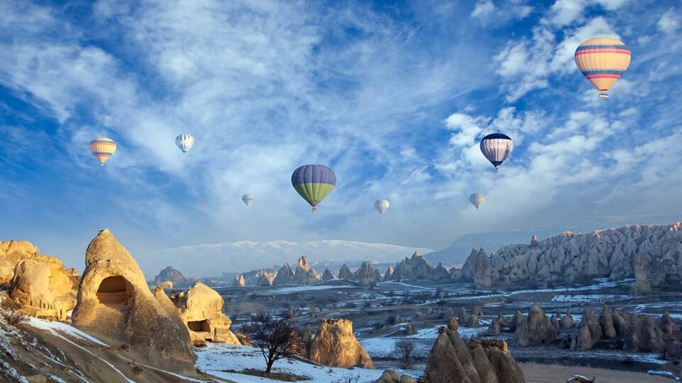 A view from the ground of many hot air balloons in the sky over a rocky landscape.
