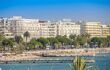Large, white seaside hotels behind a crowded beach along Cannes' seafront promenade La Croisette