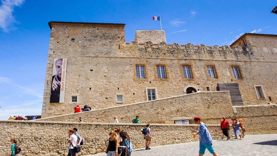 Exterior of museum in a yellow stone castle on a sunny day with visitors approaching entrance