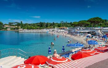 Red parasols at a beach club with blue waters and white sand beach beyond