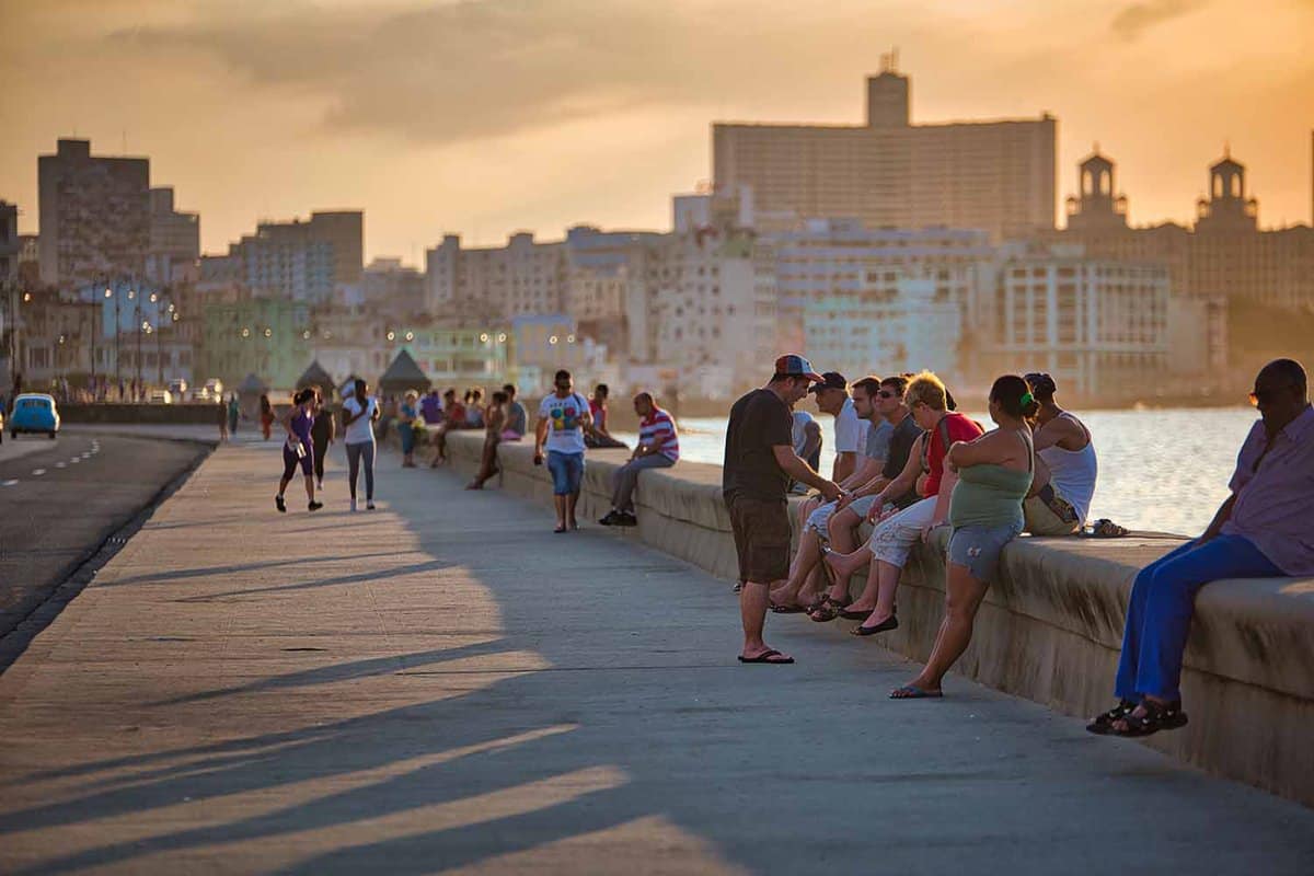 People walking and resting near the sea shore of Malecon Avenue, in the evening sunlight which reflects into Carribbean Sea, in Havana, Cuba.