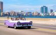 Tourists enjoying a ride on a classic american convertible car at the famous seaside Malecon avenue in Havana