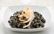 piece of cuttlefish sitting on top of a bowl of black risotto