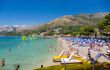 Sunny landscape side view of many people sunbathing on a beach with buildings and mountains in the background in Cavtat