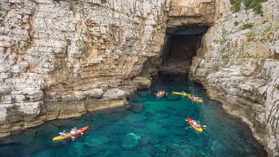 View from the rock cliffs of kayakers exploring the crystal clear Mediterranean waters of a cove off the coast of Dubrovnik, Croatia