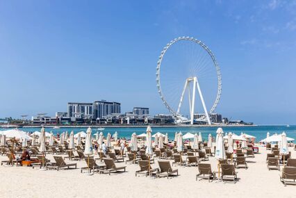Ain Dubai (Dubai Eye) tallest ferris wheel in the world on Bluewaters Island, JBR beach club with sunbeds in the foreground.