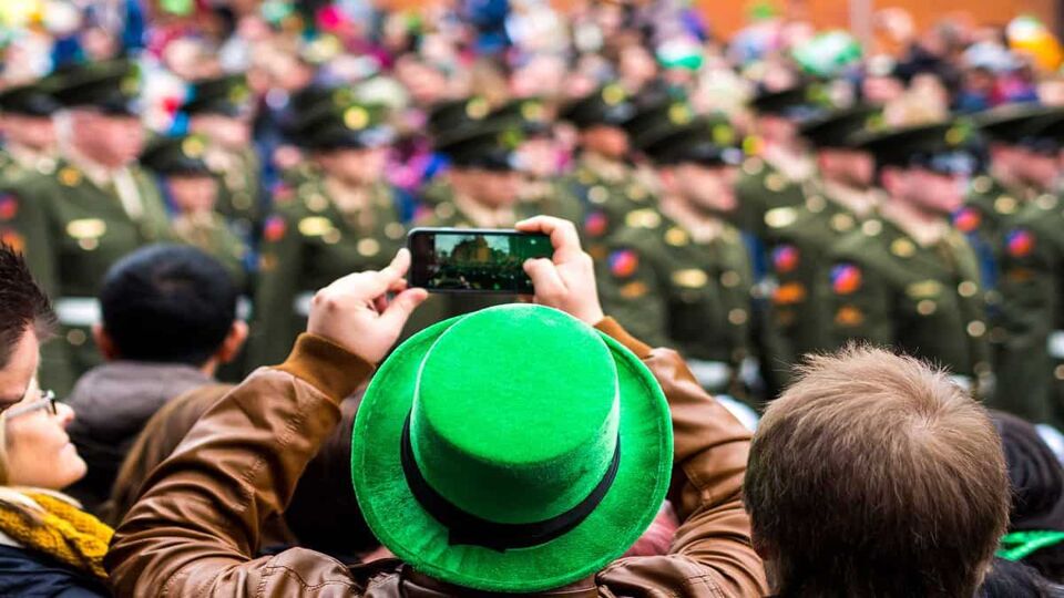 Man in bright green hat taking a photo of parade over the crowd