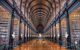 he Long Room in the Old Library at the college, a hall between rows of floor-to-ceiling old bookshelves filled with old books, with a marble bust next to each shelf