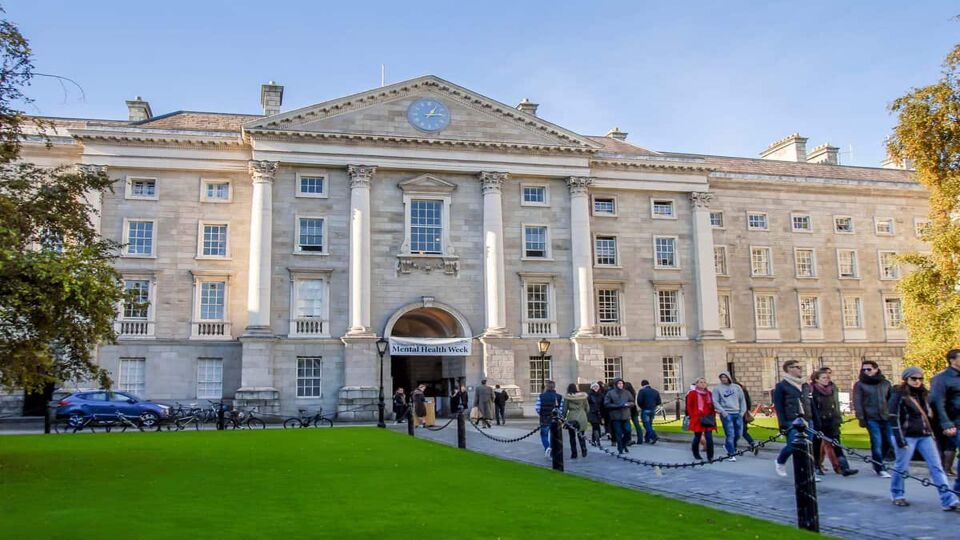 People walk down a walkway towards a large white Trinity College building