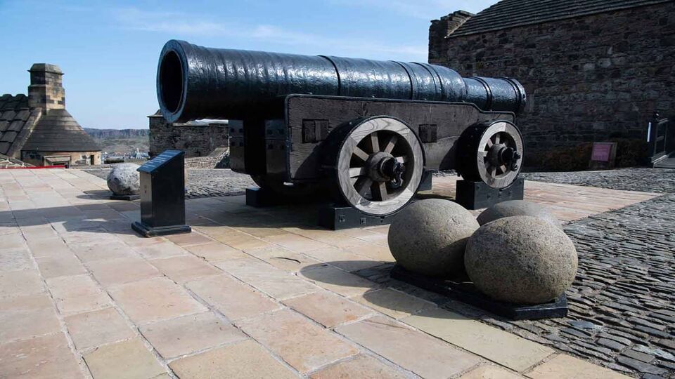 Close up of a very large black cannon with giant cannon balls in the foreground