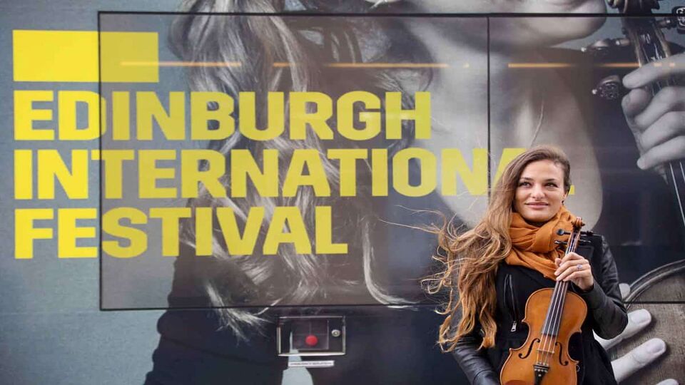 Woman standing next to billboard advertisement for Edinburgh Festival