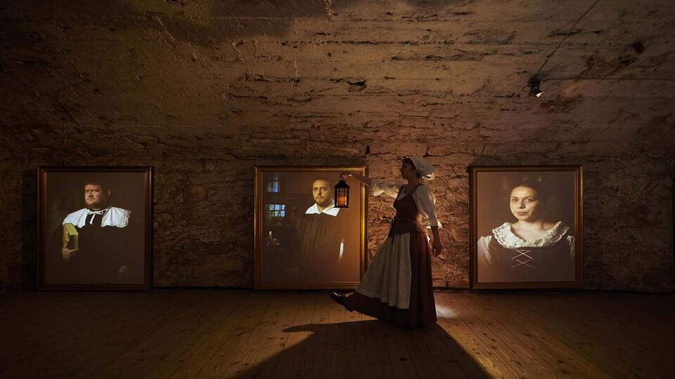 A woman dressed as old-fashioned maid walks down tunnel holding lantern