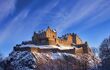 Edinburgh castle dusted with snow glows in the late afternoon blue winter sunset.