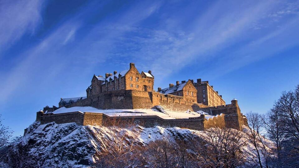 Edinburgh castle dusted with snow glows in the late afternoon blue winter sunset.