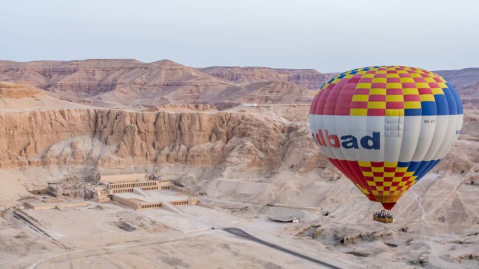View of a hot air balloon floating just above the valley containing the Temple of Hatshephsup