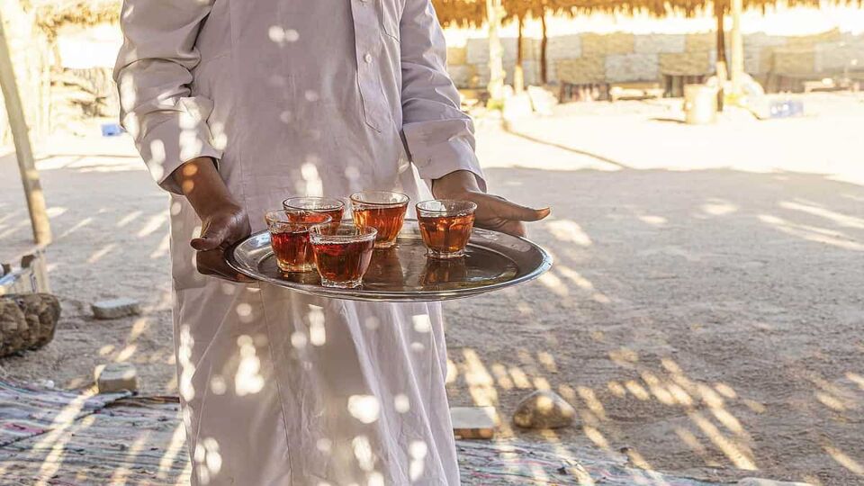 A tray with mugs of traditional Egyptian tea in the waiter's hand. Bedouin welcome a cup of tea with almonds, Sinai.